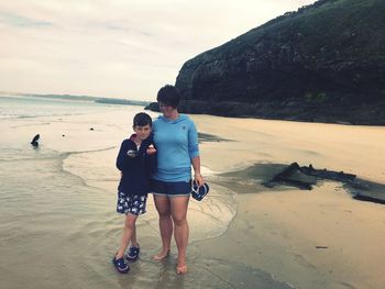 Mother and son standing on shore at beach