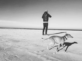 Man with dog standing on beach against sky