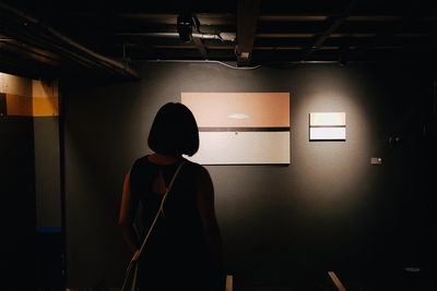 Rear view of man standing against illuminated wall