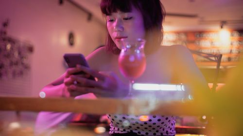 Smiling woman using mobile phone in illuminated room