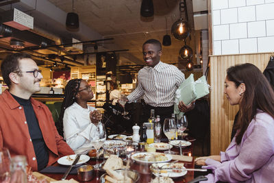 Happy man talking with male and female friends during dinner party at restaurant