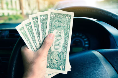 Cropped hand holding paper currencies in car