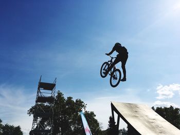 Low angle view of man jumping on umbrella against sky