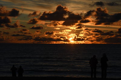 Silhouette people at beach against sky during sunset