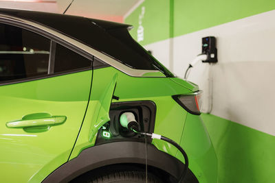 Green electric car being charged by wall at charging station