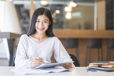 Portrait of young businesswoman using digital tablet while sitting at desk in office