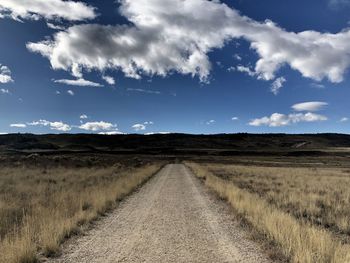 Dirt road amidst field against sky