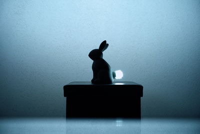 Silhouette boy sitting on table against wall