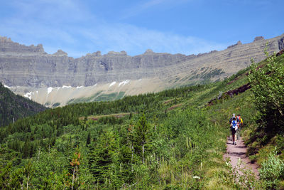 Rear view of hikers standing on mountain road against sky