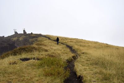 Rear view of man walking on hill against clear sky