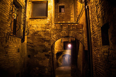 Illuminated alley amidst buildings against wall at night