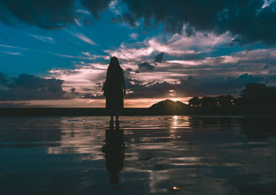 Silhouette woman standing against sea during sunset