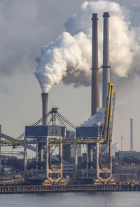 Smoke emitting from factory against cloudy sky