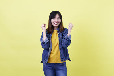Portrait of smiling young woman against yellow background