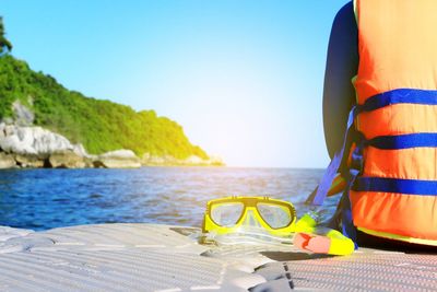 Mid section of man wearing life jacket sitting on boat in sea against clear sky