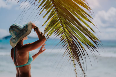 Woman wearing hat while standing by palm leaf at beach