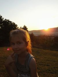 Portrait of cute girl sitting on field against clear sky during sunset
