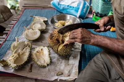 Midsection of man cutting durian on table