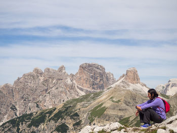 Man sitting on rock against sky