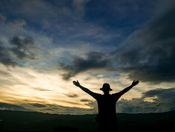 Silhouette man with arms outstretched standing against sky during sunset