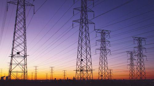 Low angle view of electricity pylon against sky at sunset