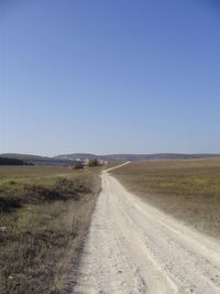 Road amidst field against clear sky