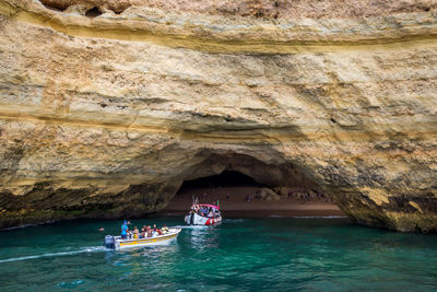 People in boats on sea against cliff