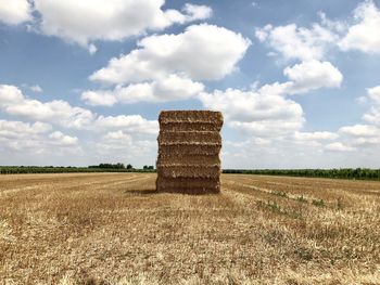 Stack of hay bales on field against sky