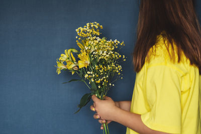 Midsection of woman holding bouquet against clear blue sky