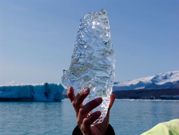 Cropped image of hand holding ice against sea