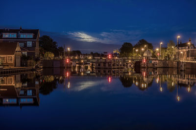 Illuminated cityscape by river against sky at night