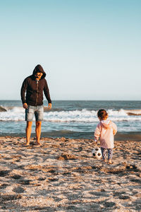 Father and daughter playing at beach against clear sky