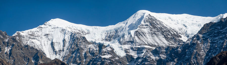 Panoramic view of snowcapped mountains against clear blue sky