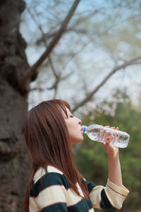 Side view of mid adult woman drinking water while standing in park