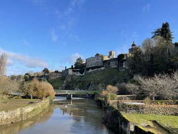 Arch bridge over river by buildings against sky