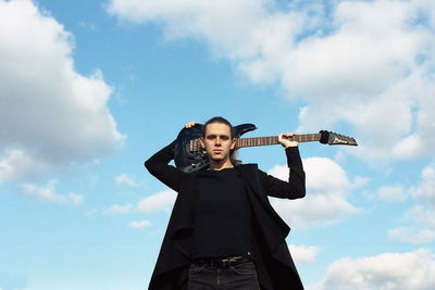 Low angle portrait of young man holding guitar against sky