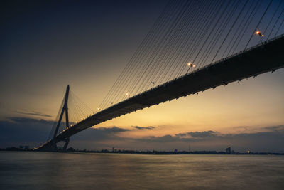 View of suspension bridge over river against cloudy sky