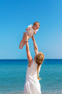 Rear view of woman standing at beach against clear blue sky