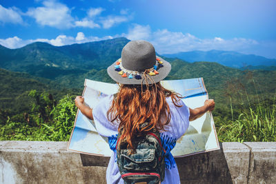 Rear view of woman with hat standing against mountains