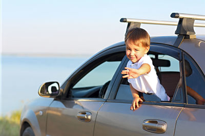 Side view of boy in car against sky