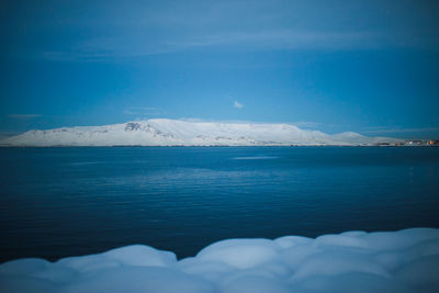 Scenic view of sea and snowcapped mountains against blue sky