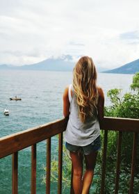 Rear view of woman standing by railing against sea