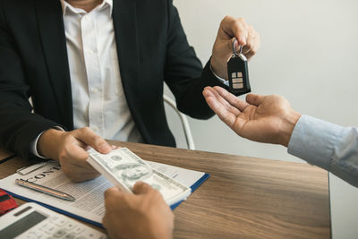 Midsection of man receiving money while giving car key to customer on table