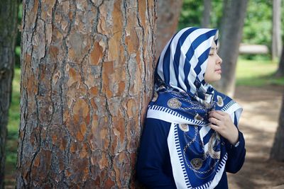 Woman in hijab standing by tree trunk