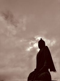 Low angle view of silhouette buddha statue against cloudy sky during sunset