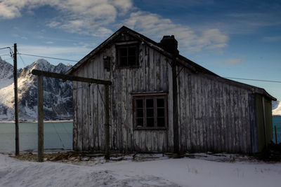 Abandoned house on snow covered field against sky