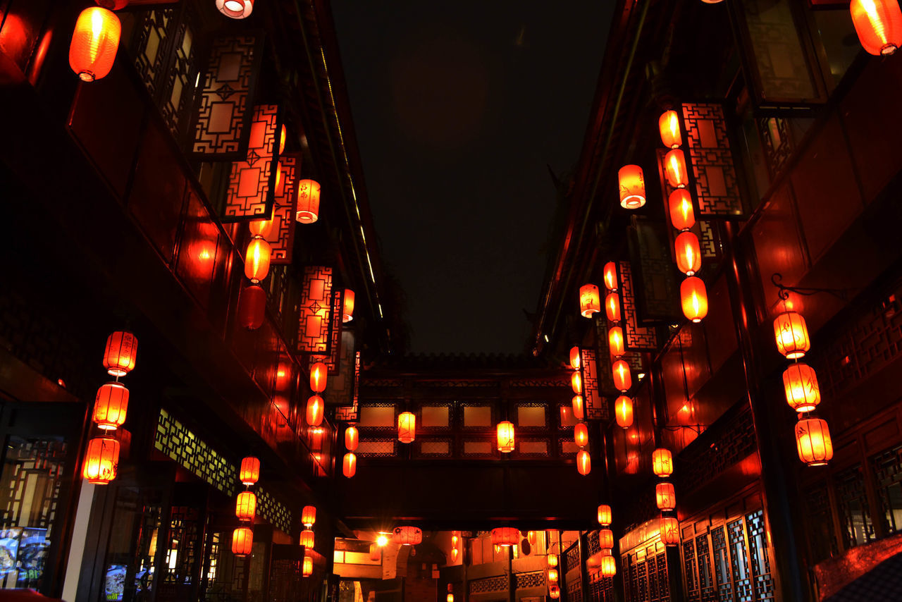 LOW ANGLE VIEW OF ILLUMINATED LANTERNS HANGING AMIDST BUILDINGS