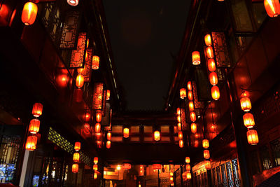 Low angle view of illuminated lanterns hanging amidst buildings at night