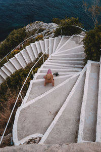 High angle view of woman sitting on staircase by sea