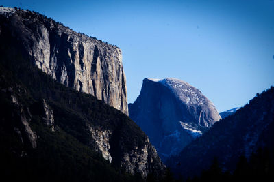Low angle view of snowcapped mountains against clear blue sky